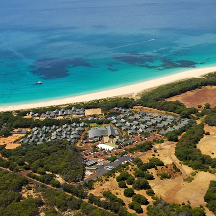 An aerial view of a coastal resort with multiple buildings, a beach, and surrounding greenery.