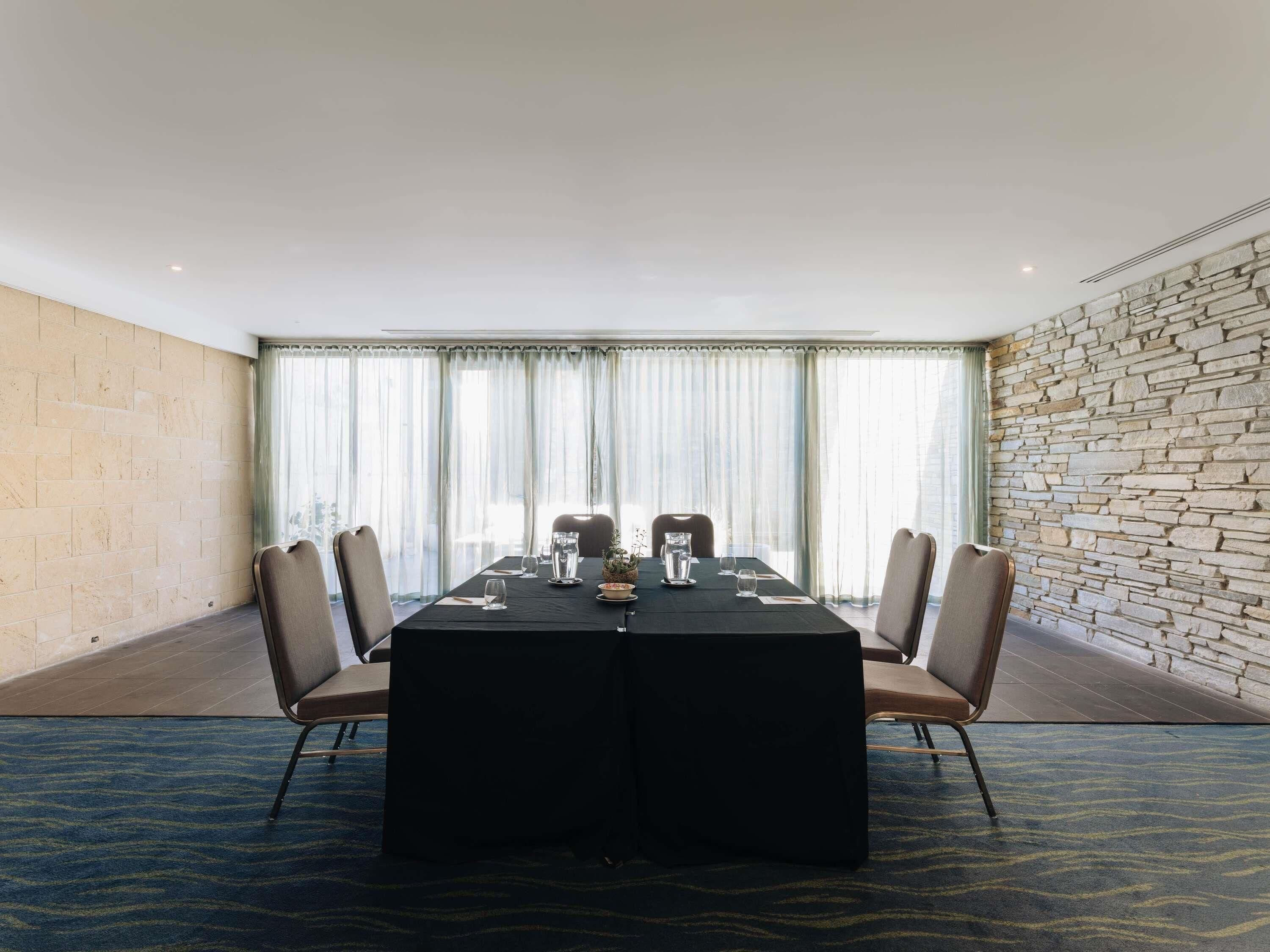 Un salón de conferencias con una larga mesa, sillas y una pared de piedra.