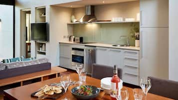 Una cocina moderna con electrodomésticos integrados, un comedor con mesa de madera lista para una comida, y una sala de estar con sofá y televisor.