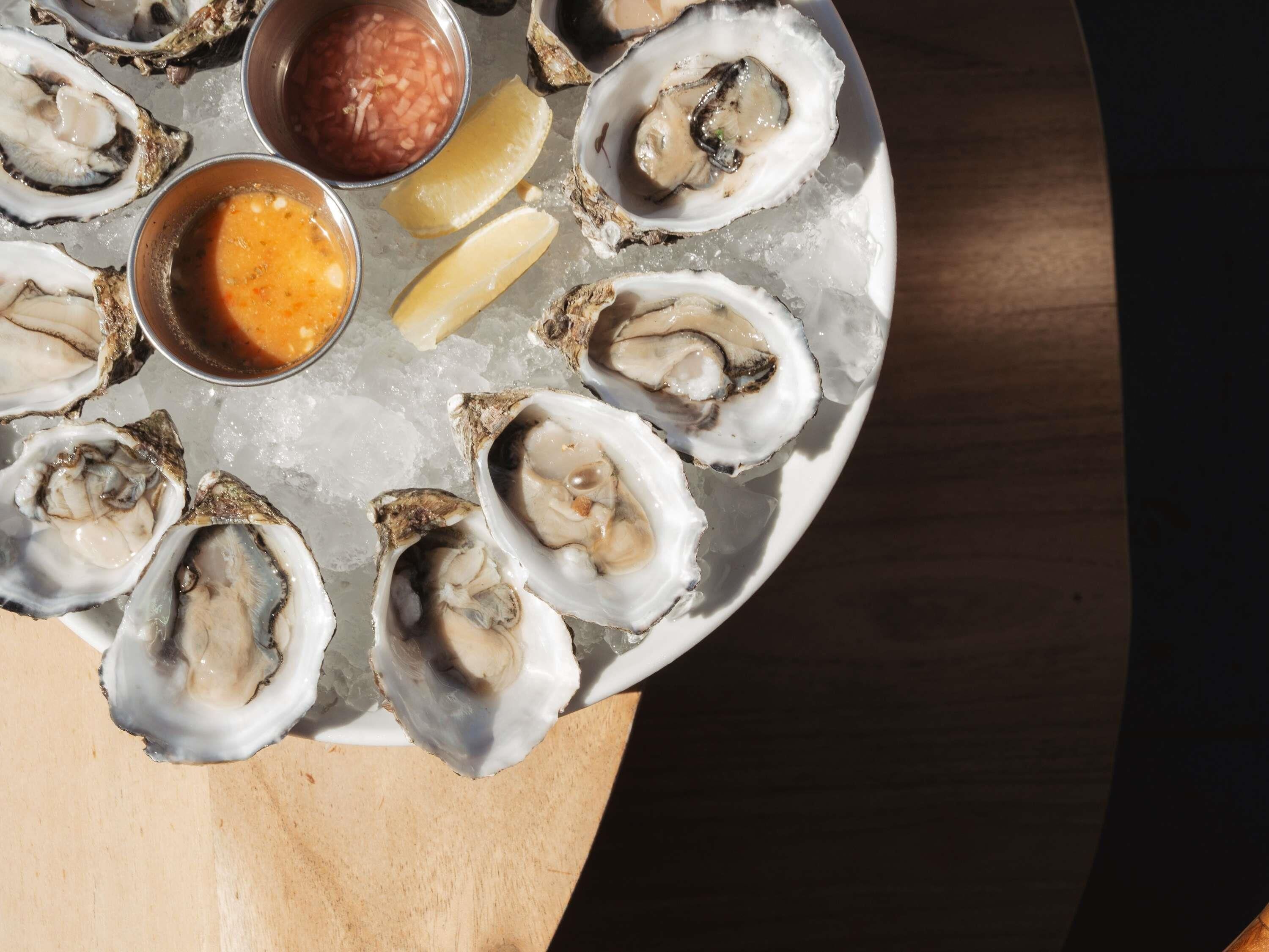 A plate of oysters with lemon wedges and two sauces.