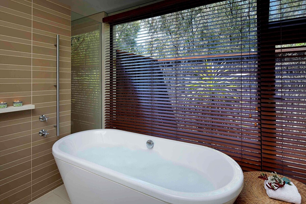 Une salle de bain moderne avec une baignoire sur pieds, une douche en verre et une fenêtre avec des stores.
