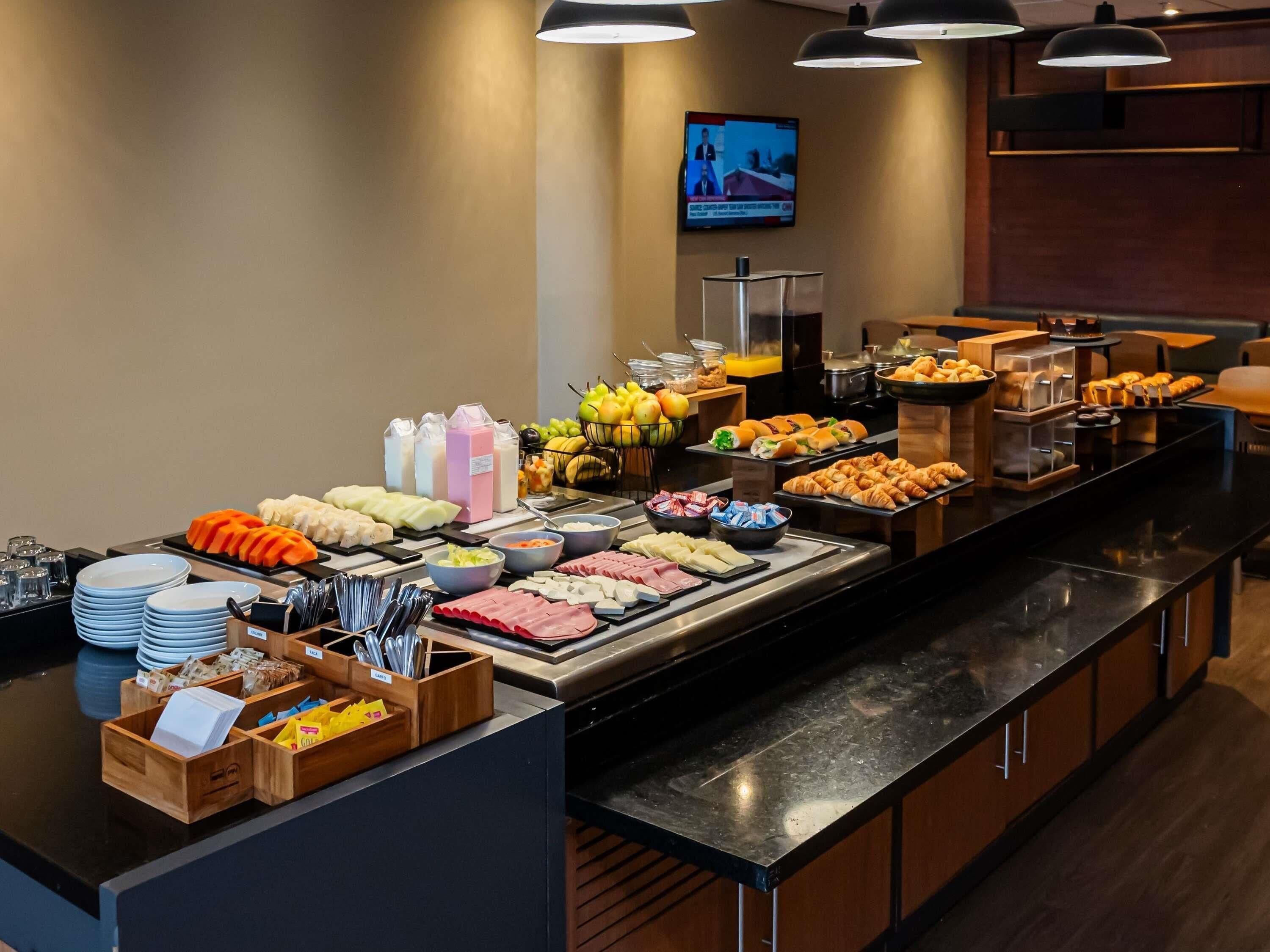 A buffet with various food items, utensils, and a television screen in the background.