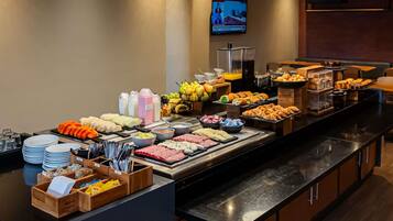 A buffet with various food items, utensils, and a television screen in the background.