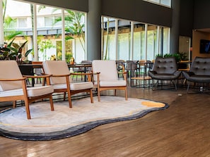Un espacio interior moderno con asientos de madera y cuero, un tapete estampado y grandes ventanales con vistas al exterior.