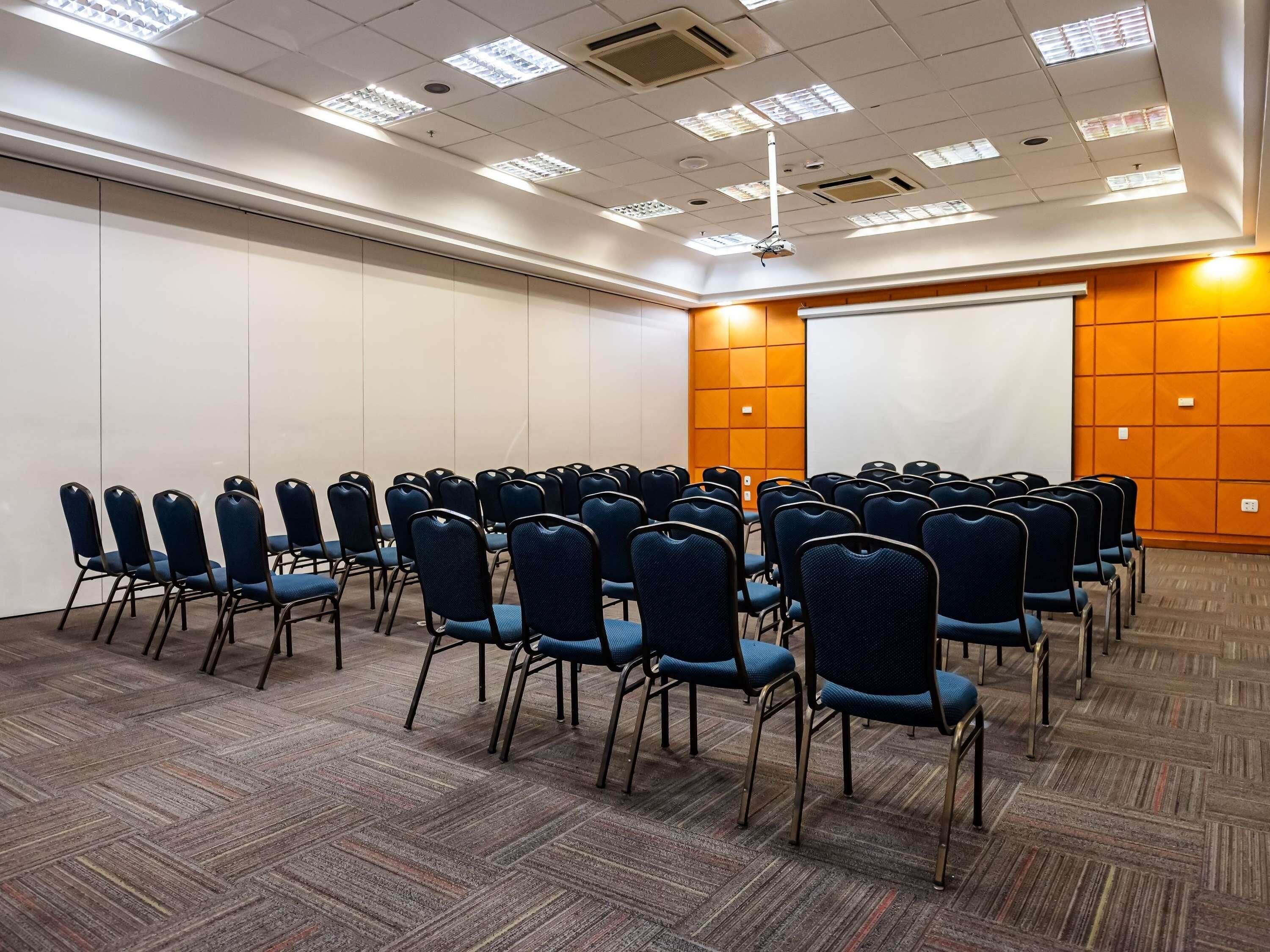 Una sala conferenze con file di sedie, uno schermo per proiezioni e una lavagna.
