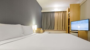 Ein Hotelzimmer mit einem großen Bett, einem Fernseher und einem Fenster mit Vorhängen.