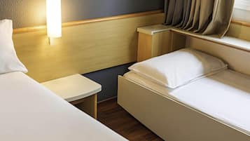 A hotel room with two beds, a bedside table, a lamp, and a window with curtains.