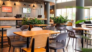 Ein modernes Café-Interieur mit Holztischen und -stühlen, einer Rezeption und großen Fenstern, die viel Tageslicht hereinlassen.