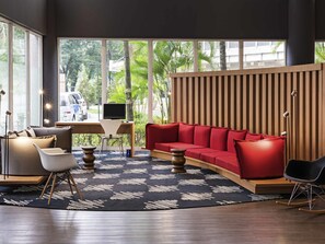 A modern hotel room with a large window, a red sofa, a desk with a computer, and a wooden slatted wall. - ibis Santo Andre (Santo André)