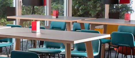 Un comedor moderno con sillas color turquesa y mesas de madera, con lámparas negras y rojas.