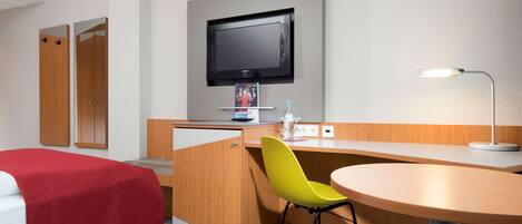 Una habitación de hotel con una cama, un escritorio con una silla, un televisor y una lámpara.