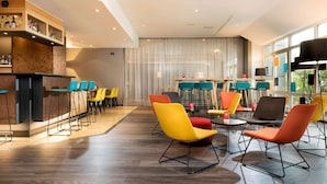 A modern hotel lobby with a bar area, multiple seating options, and large windows. - Ramada by Wyndham Hannover (Laatzen)