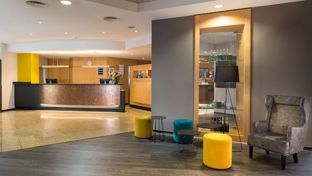 A modern lobby with a reception desk, seating areas, and a glass display case. - Ramada by Wyndham Hannover (Laatzen)