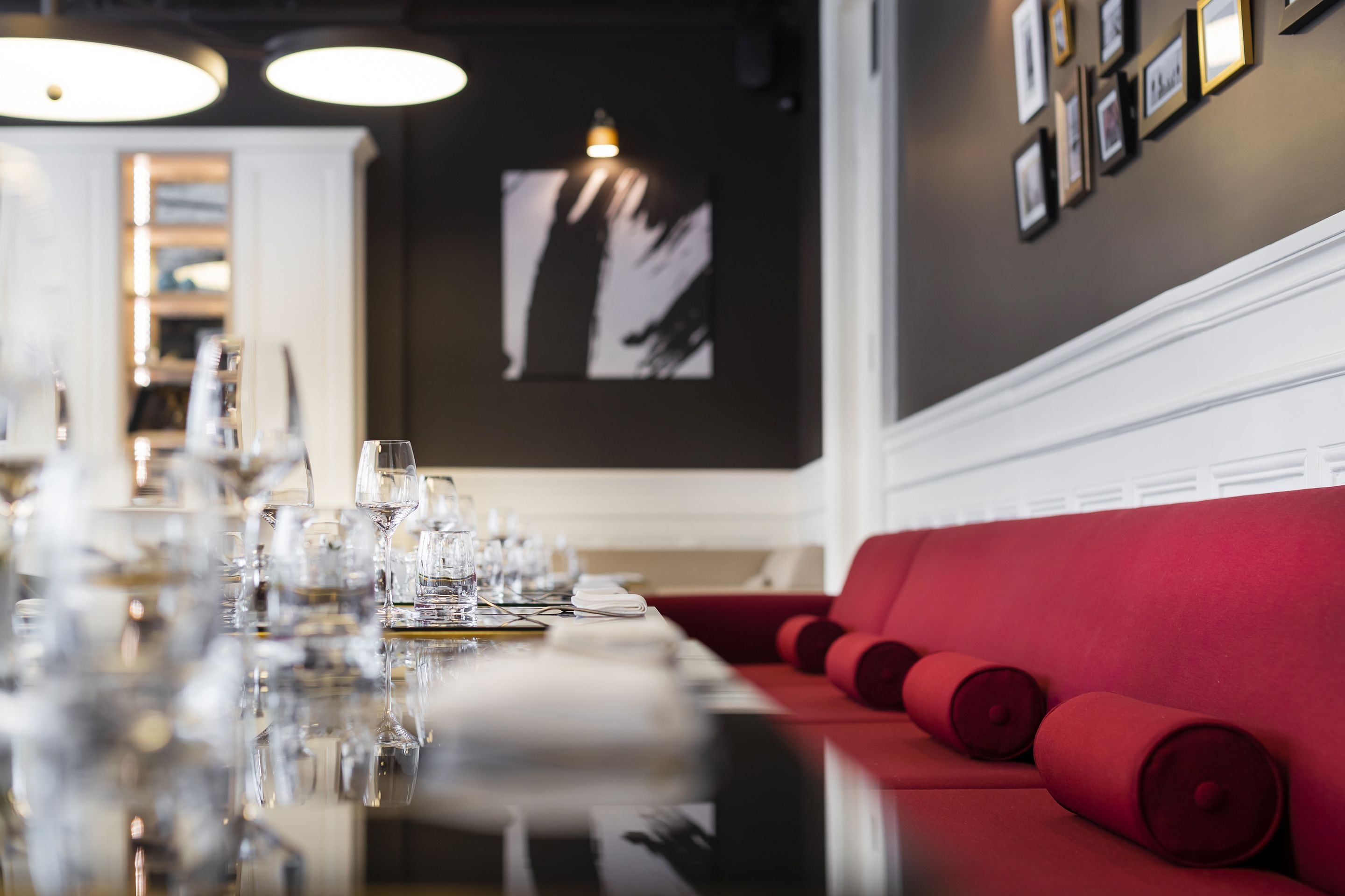 Une table à manger dressée avec des verres et des assiettes, un canapé rouge et des tableaux encadrés accrochés au mur.