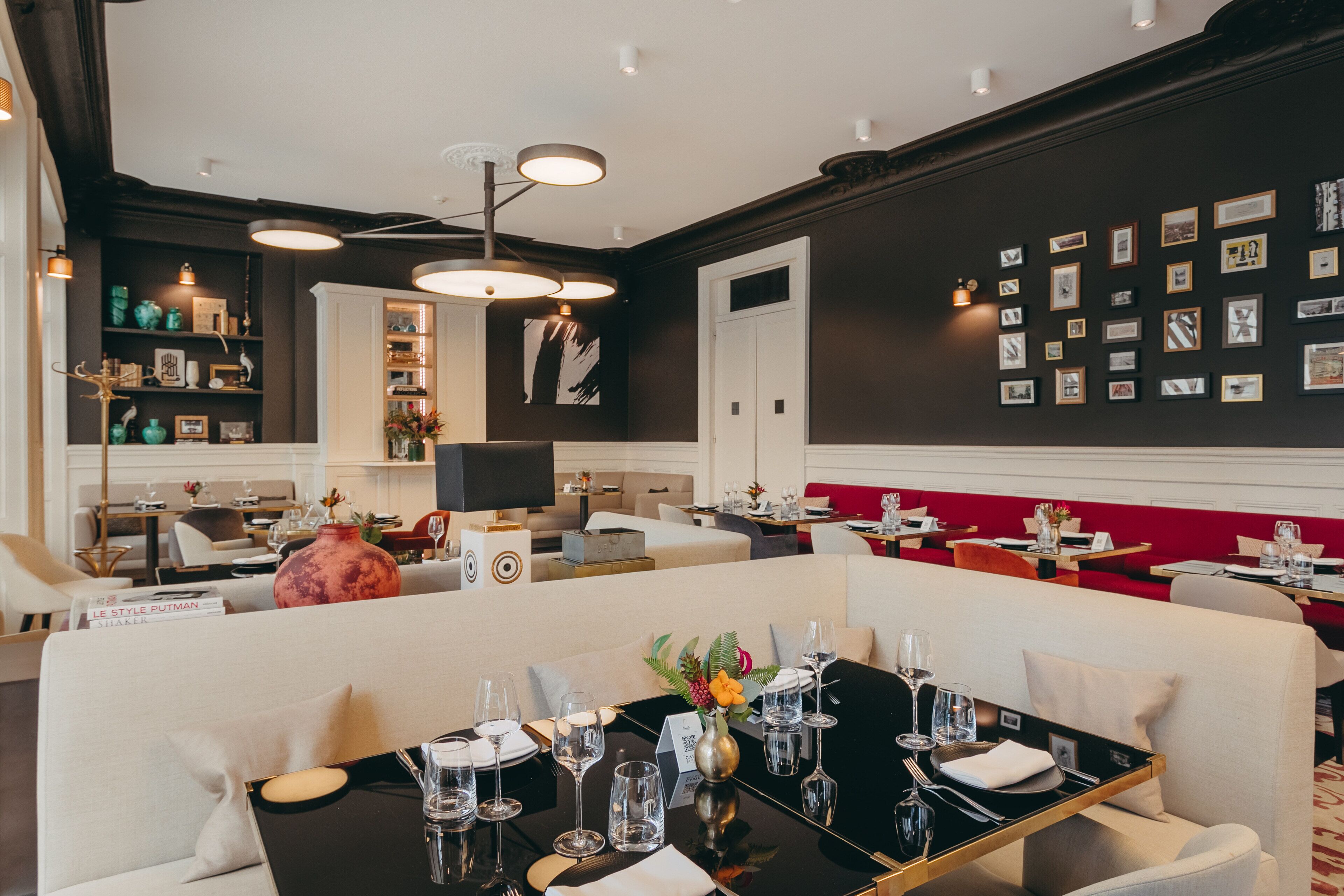 Un restaurante moderno con una paleta de colores blanco y negro, que presenta un área de comedor con mesas preparadas para el servicio, una zona de bar y una pared decorada con fotografías enmarcadas.
