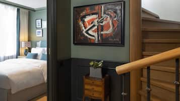 Una habitación de hotel con una cama, una mesita de noche con un florero y una pintura en la pared, además de una escalera.