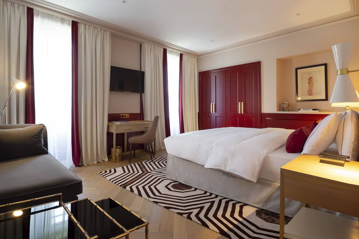 A hotel room with a bed, a desk, a chair, a TV, and a lamp.