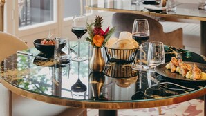 A dining table with a glass top, surrounded by chairs, a bowl of food, wine glasses, and a vase with flowers. - Hôtel Longemalle (Geneva)