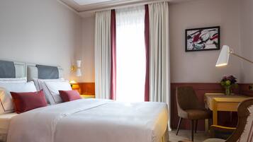 Una habitación de hotel con una cama grande, un escritorio, una silla, una lámpara y un cuadro en la pared.
