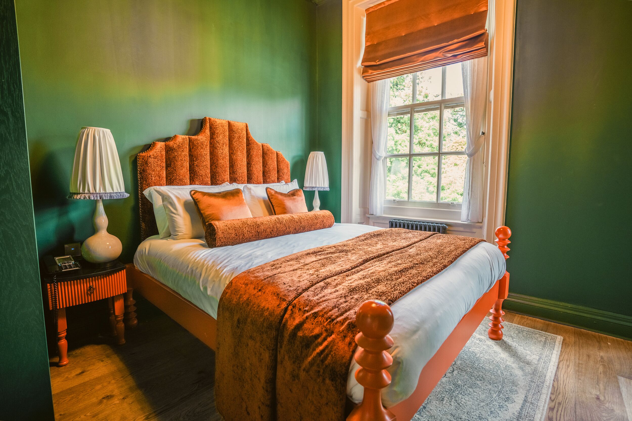 A bedroom with a bed, two bedside tables, a window with a view, and a green wall.
