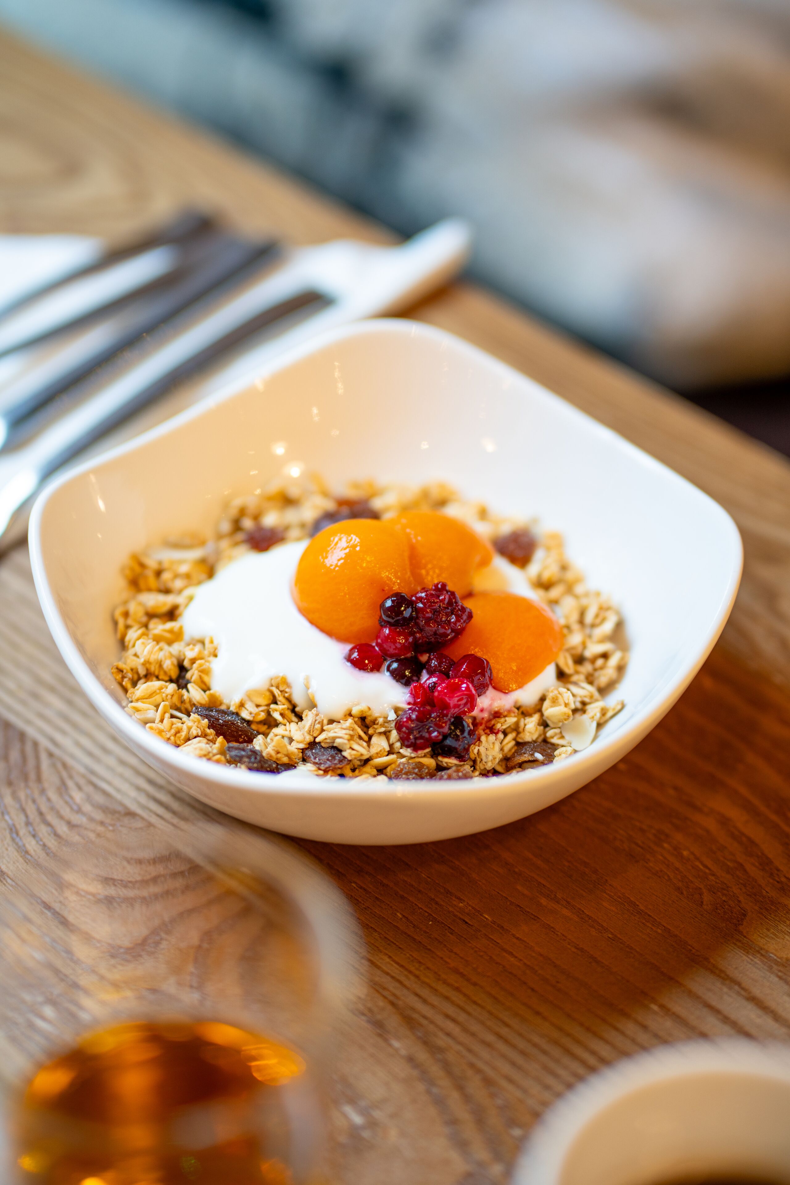 A bowl of granola with fruit and yogurt on a wooden table.