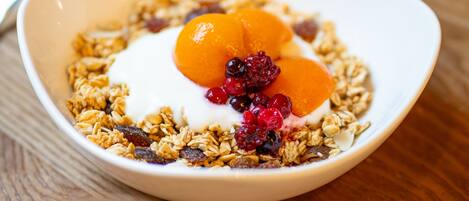 A bowl of granola with fruit and yogurt on a wooden table.