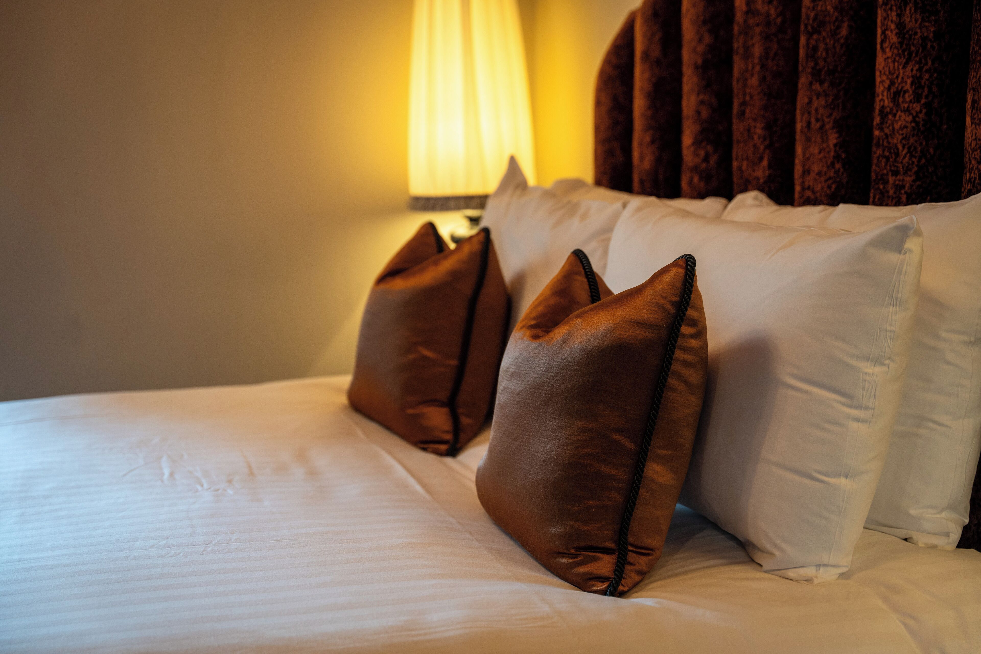 A neatly made bed with white linens and two brown pillows.