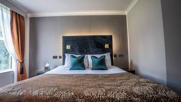 A hotel room with a large bed, a headboard with two light switches, and a window with curtains.