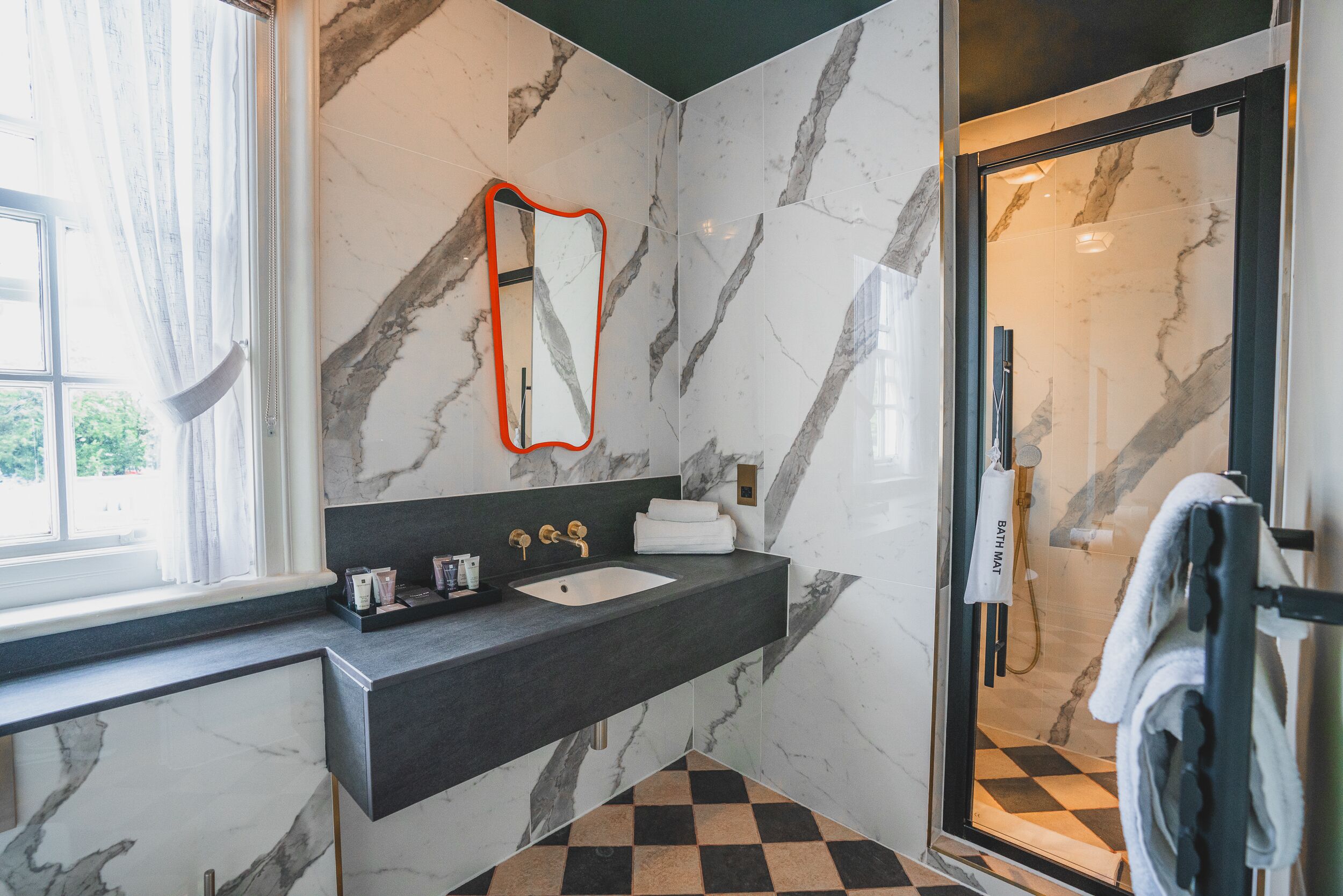 A modern bathroom with a marble wall, a black countertop, a sink, a mirror, and a shower area.