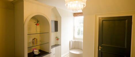 A hallway with a glass display case, a round white chair, and a dark door.