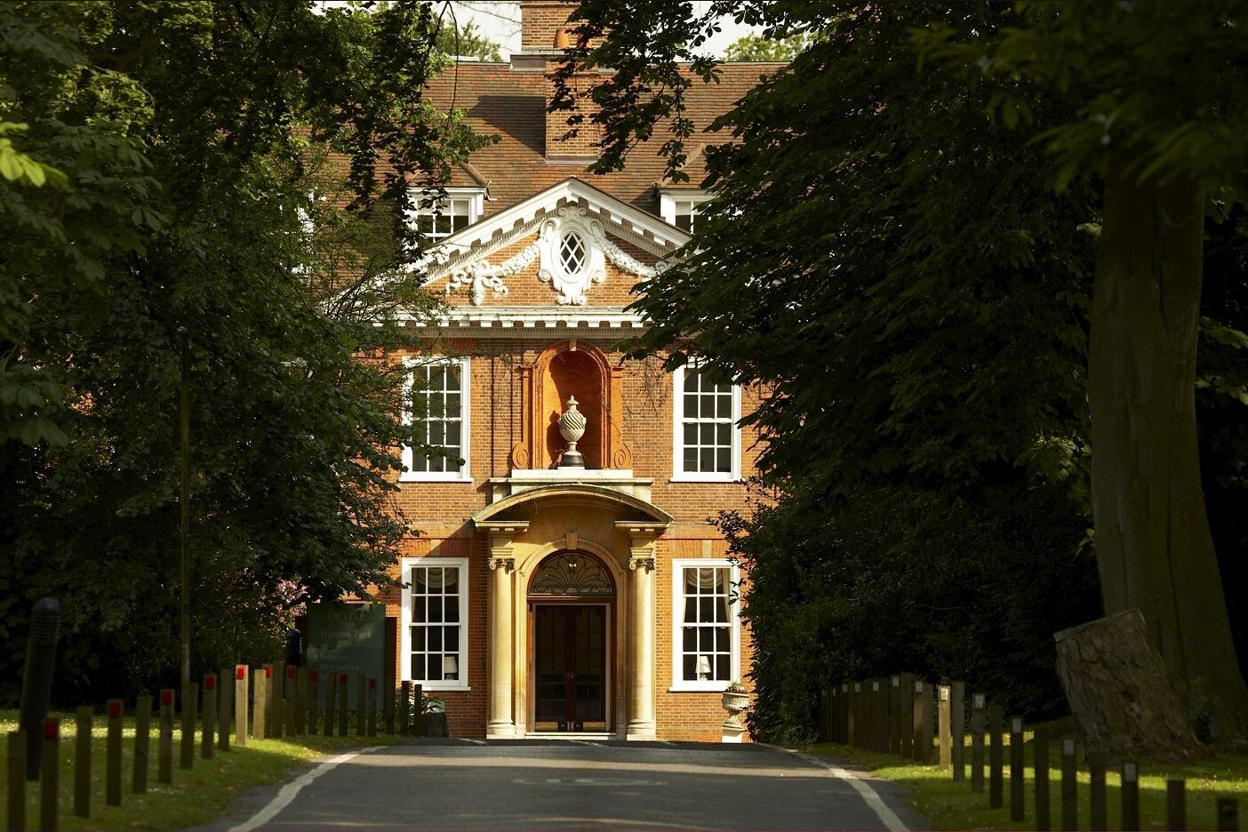 A traditional brick building with a central entrance, flanked by trees and a paved driveway.
