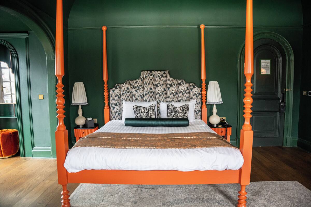 A four-poster bed with a patterned headboard, white bedding, and two bedside tables with lamps.