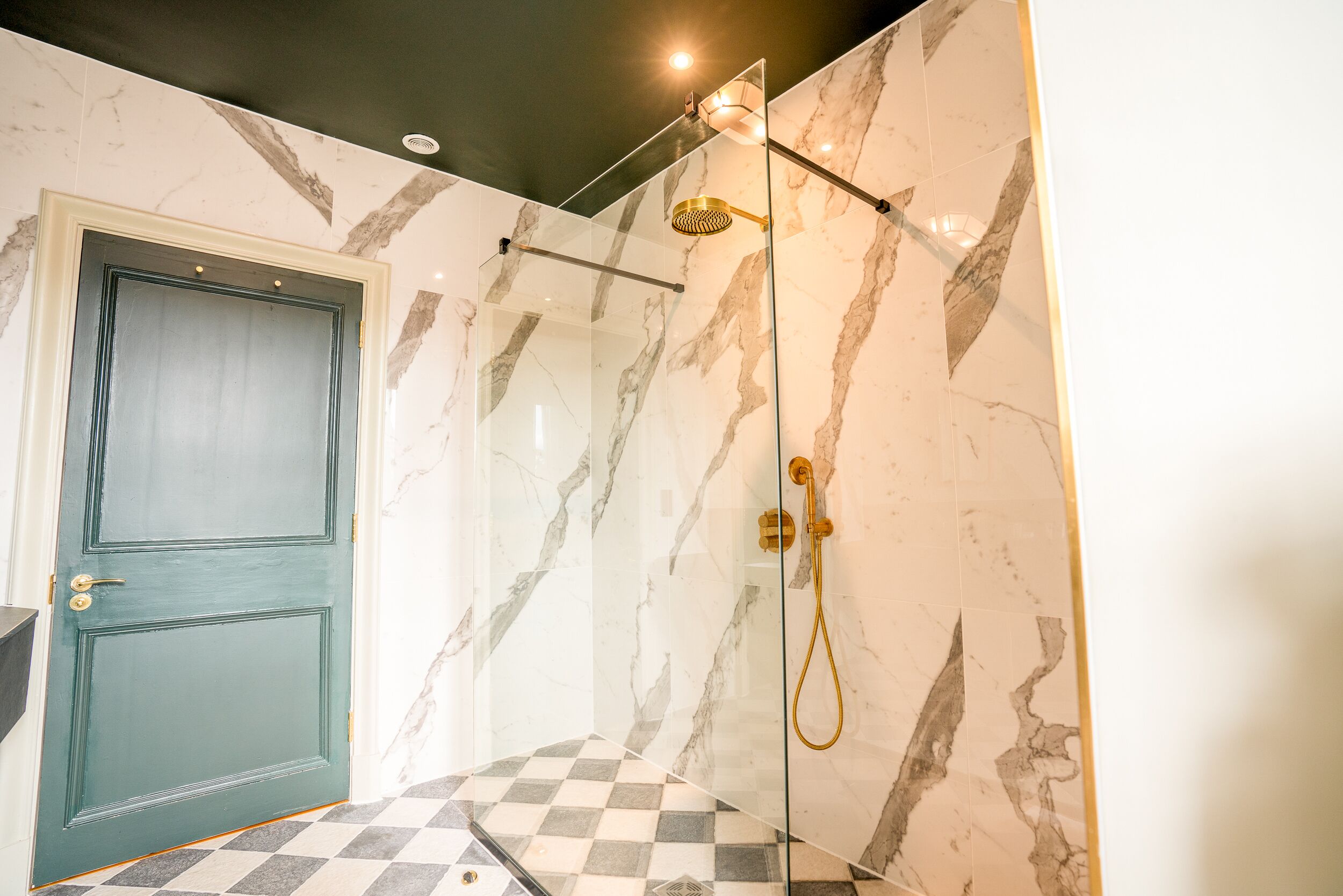 Un baño moderno con ducha de vidrio, paredes de mármol y piso de baldosas a cuadros.