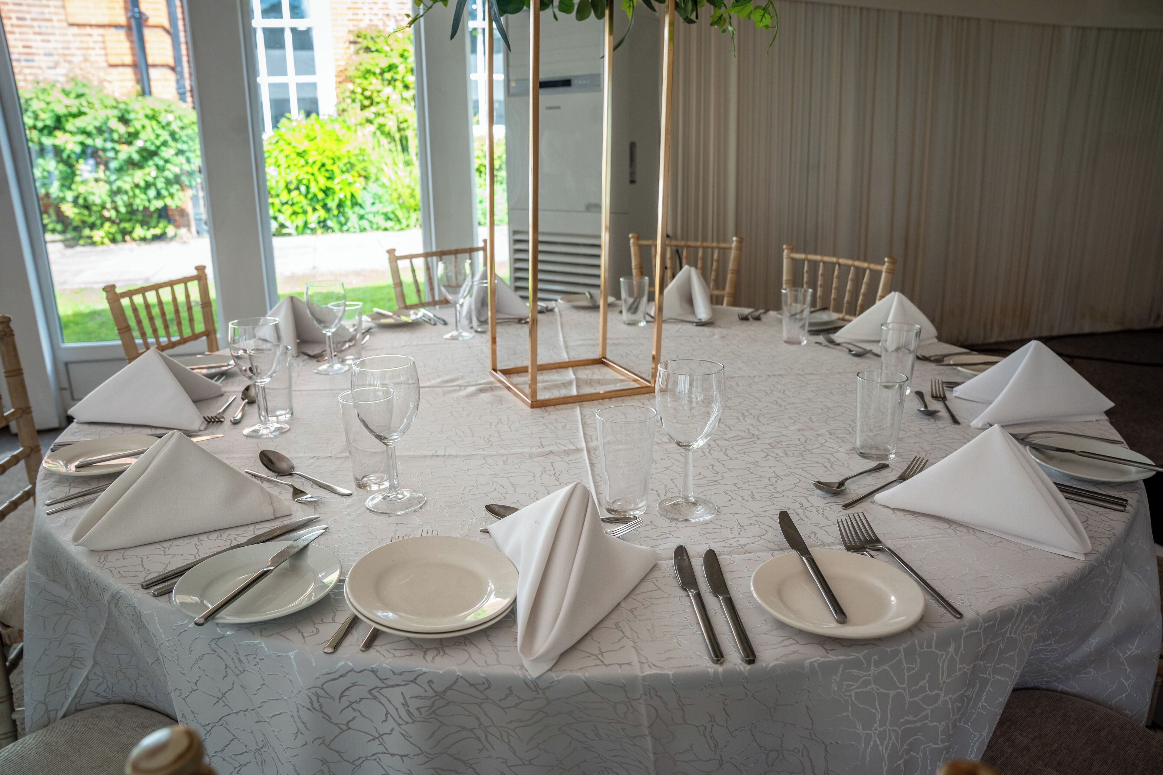 A round table set for a formal event with white tablecloths, folded napkins, and silverware.