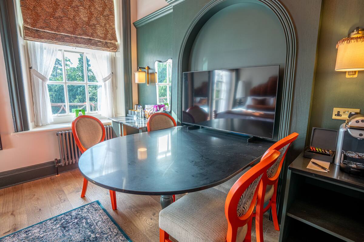 A dining area with a round table, chairs, a television, and a coffee machine.