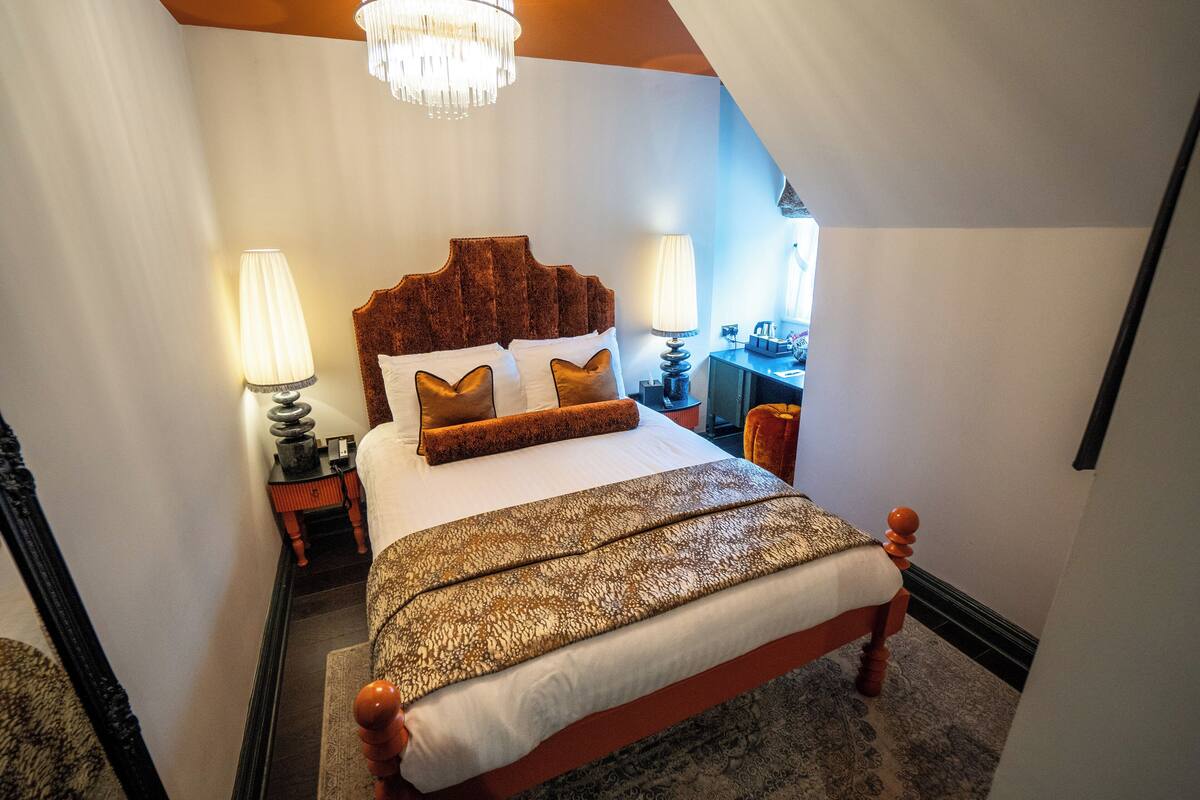 A bedroom with a large bed, two bedside lamps, a chandelier, and a desk with a chair.