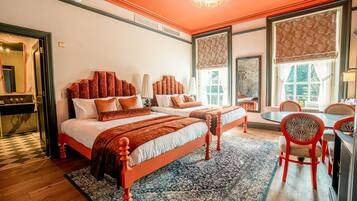 A hotel room with two beds, a dining area, and large windows.