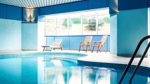 Una piscina interior con agua azul cristalina, rodeada de paredes azules y un ventanal grande.