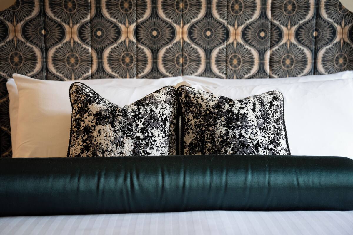 A bed with a patterned headboard, a white pillow, and a dark green bedspread.