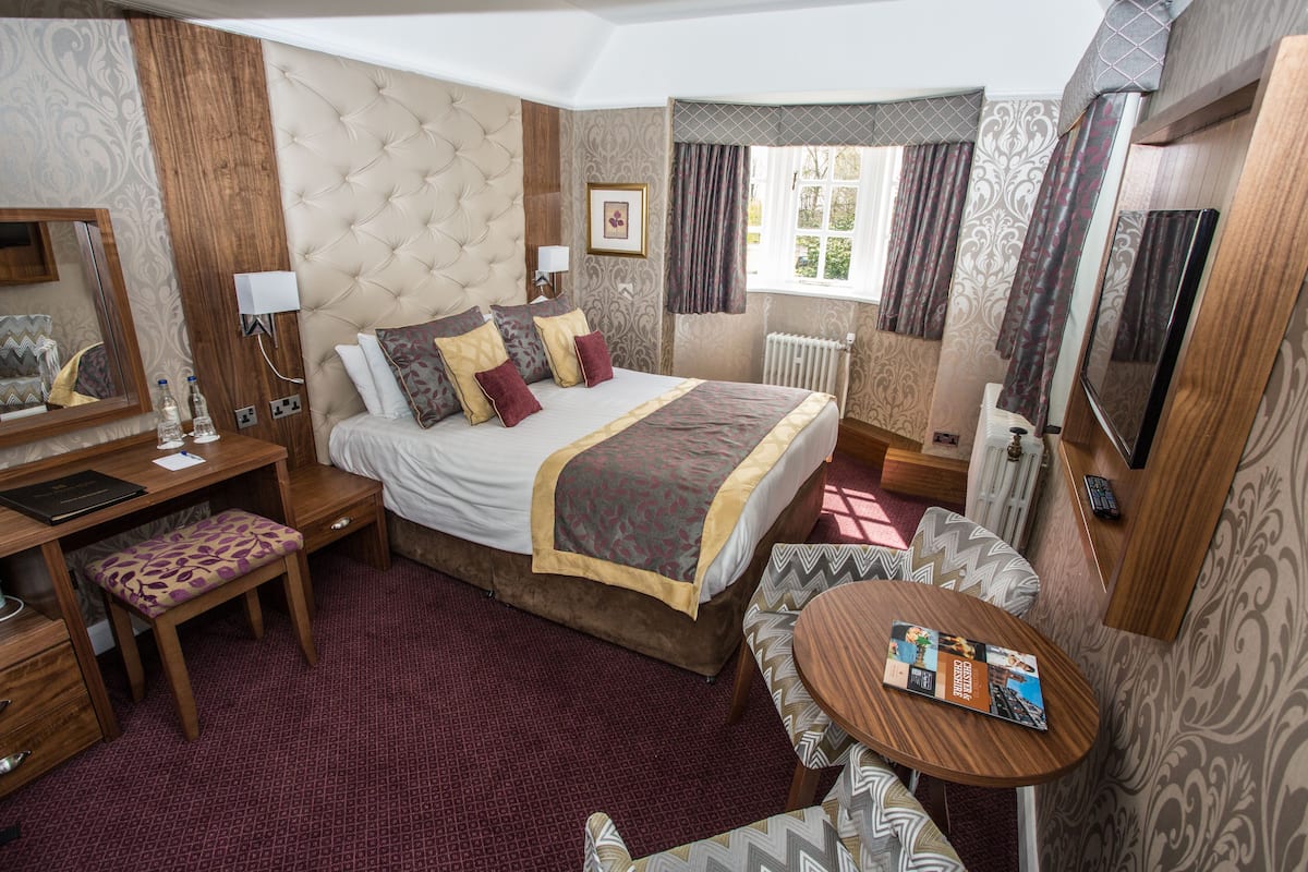 A hotel room with a large bed, a desk, a chair, a small table, and a mirror.