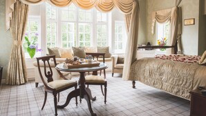 Un dormitorio con una cama grande, una mesa redonda con sillas, una ventana con cortinas y un candelabro.
