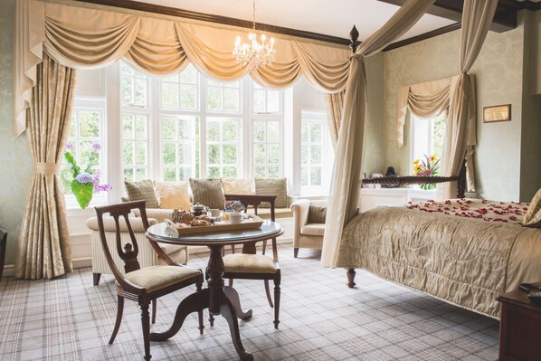 A bedroom with a large bed, a round dining table with chairs, a window with curtains, and a chandelier. - Mere Court Hotel (Knutsford)