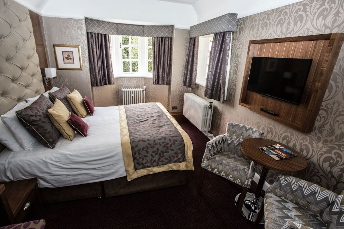 A hotel room with a large bed, a television, a sofa, and a window with curtains.