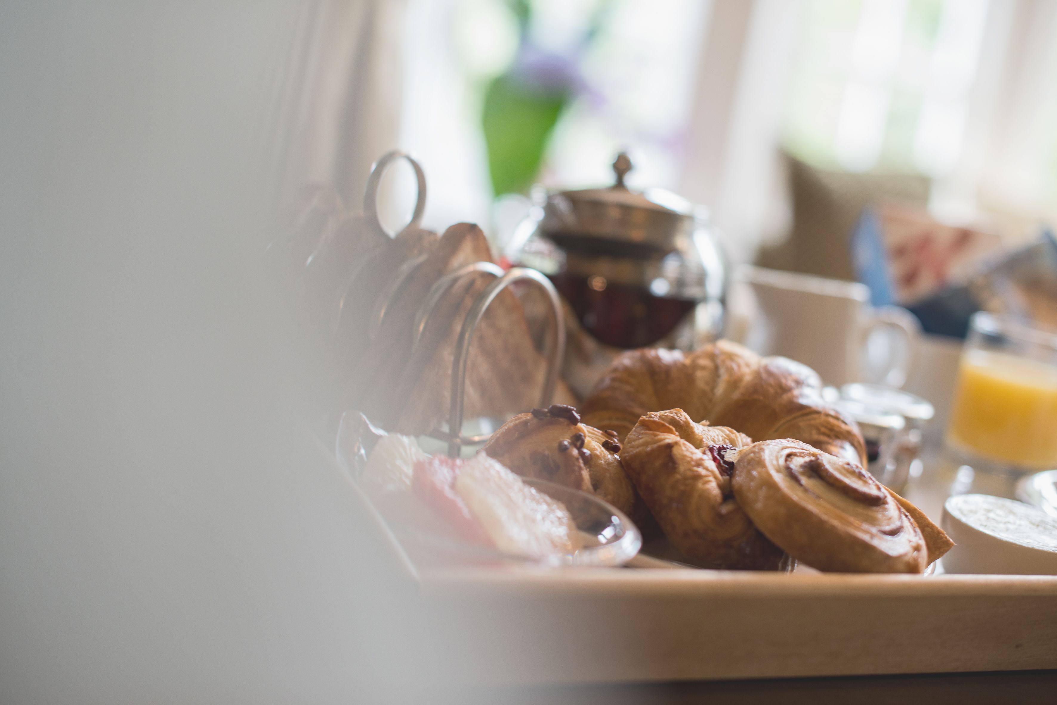 A breakfast tray with croissants, a teapot, and a glass of orange juice.