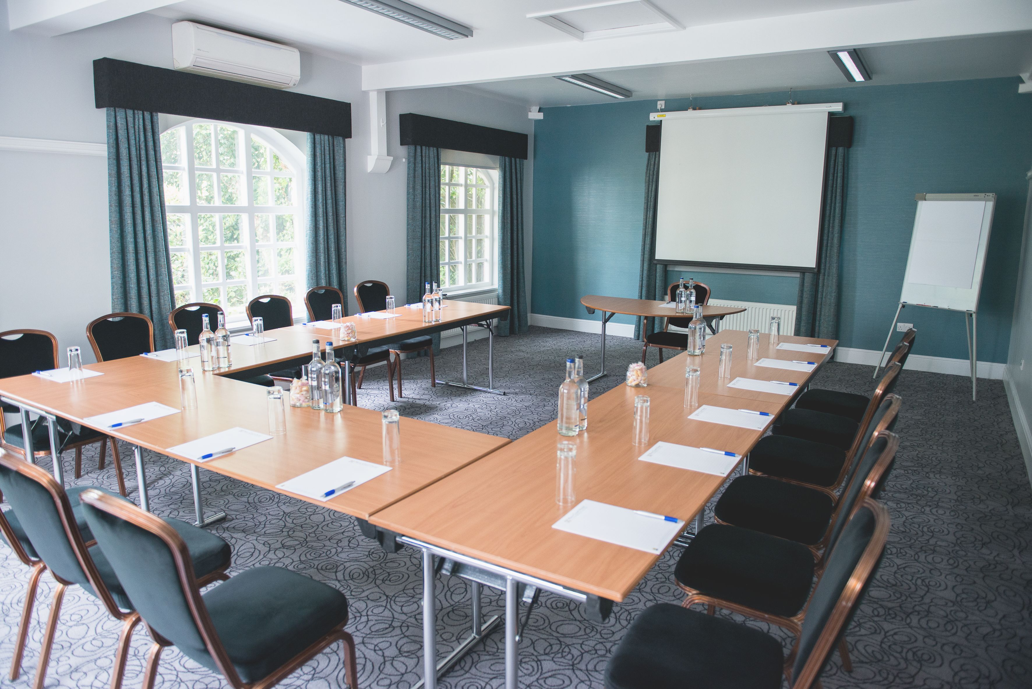 Ein Konferenzraum mit langem Tisch, Stühlen, einer Projektionsleinwand und einer Wandtafel.