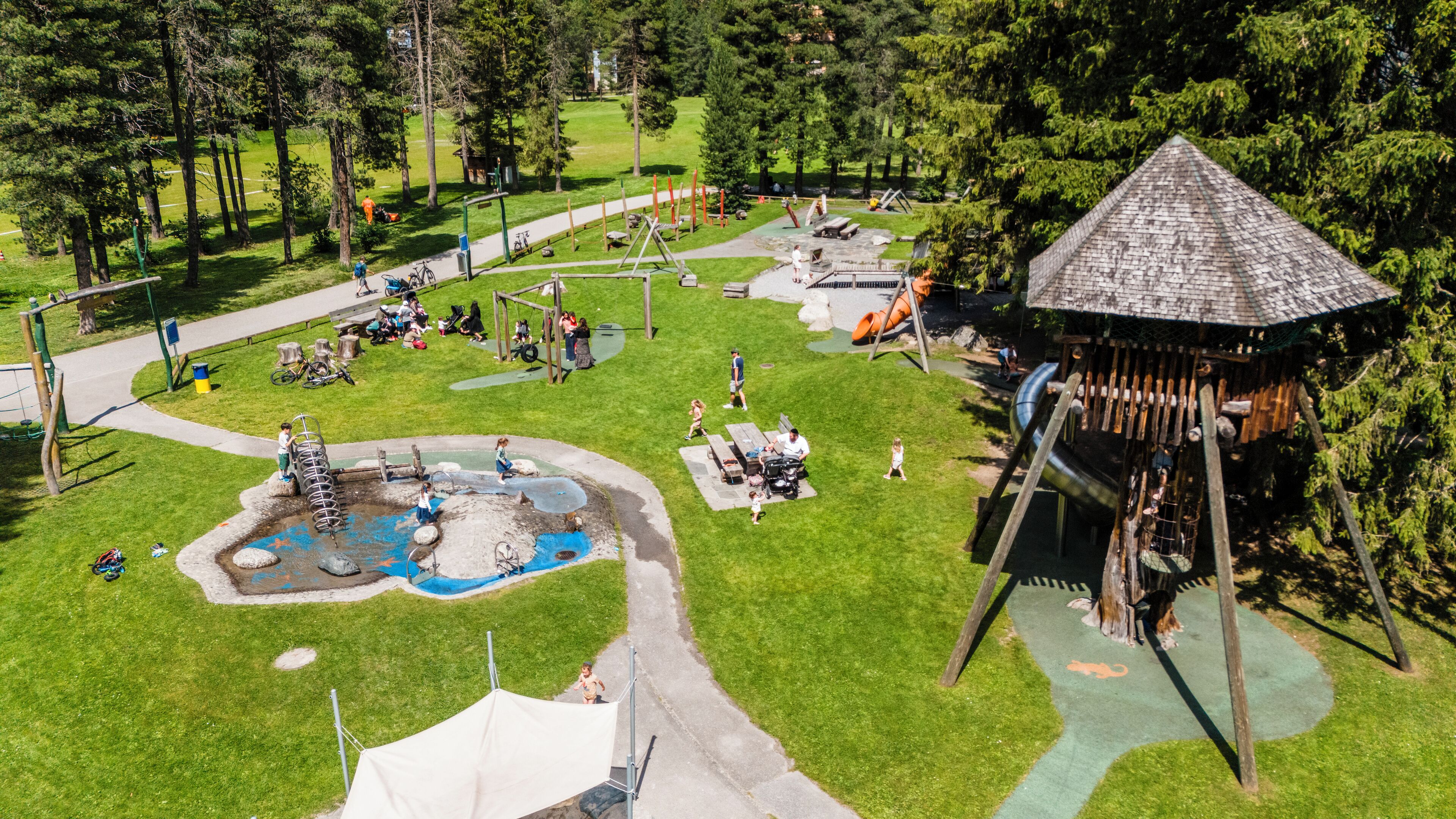A playground with various play structures, a small water feature, and a covered seating area.
