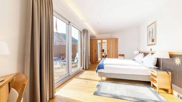 Een hotelkamer met een grote schuifpui die leidt naar een balkon, een bed met nachtkastje, een bureau en een stoel.