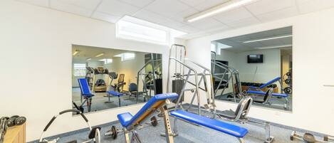 A gym with exercise equipment, mirrors, and a blue bench.