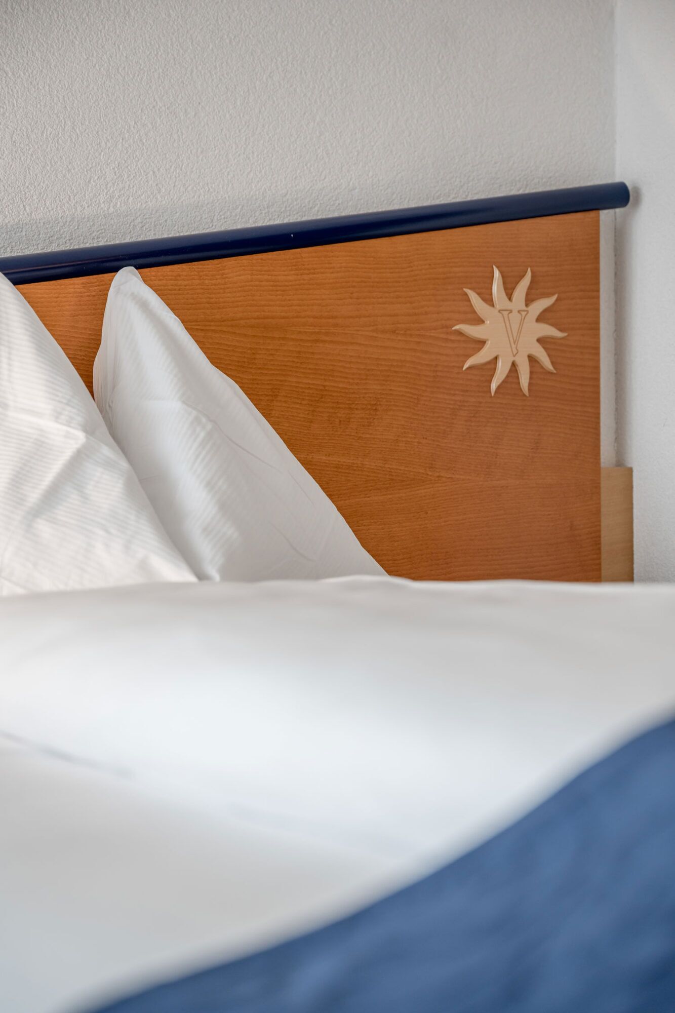 A bed with white bedding, a wooden headboard with a sun-like design, and a dark blue headboard rail.