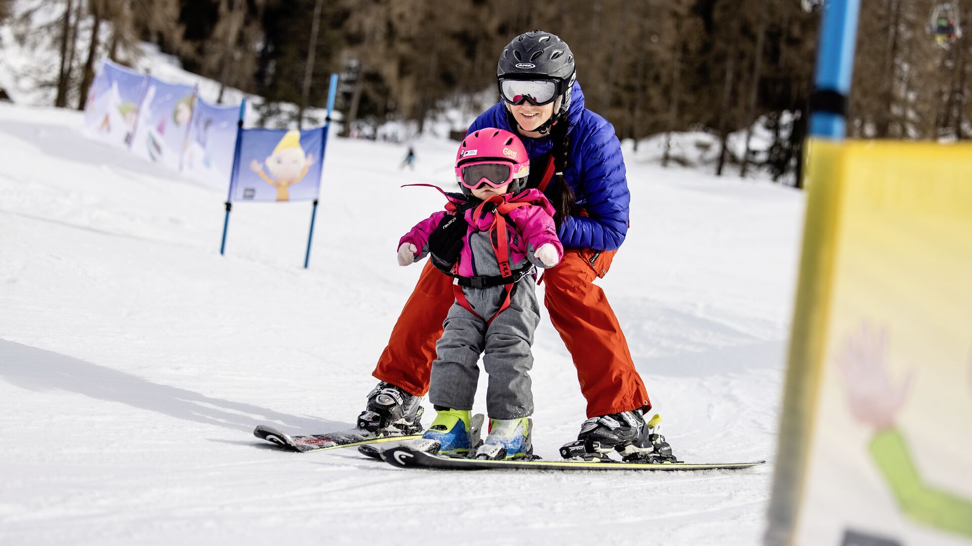 A snowy ski slope with a person skiing and a child in ski gear.